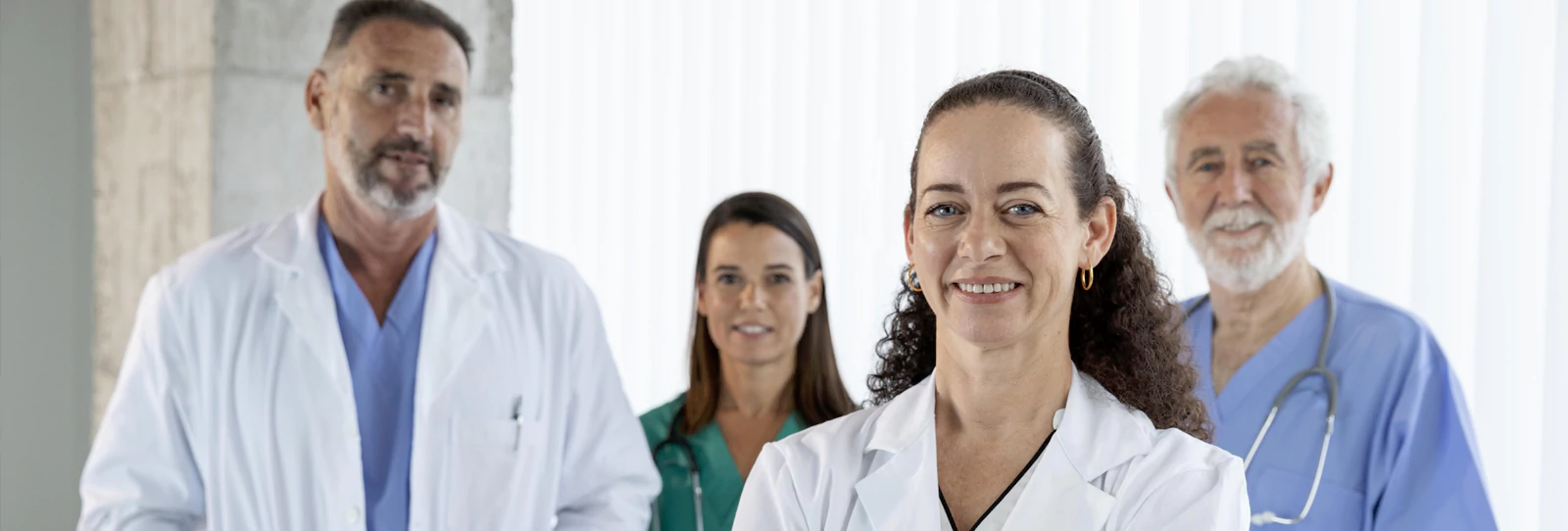Three people at a round table working with a laptop, tablet, and smartphone alongside charts and notes.